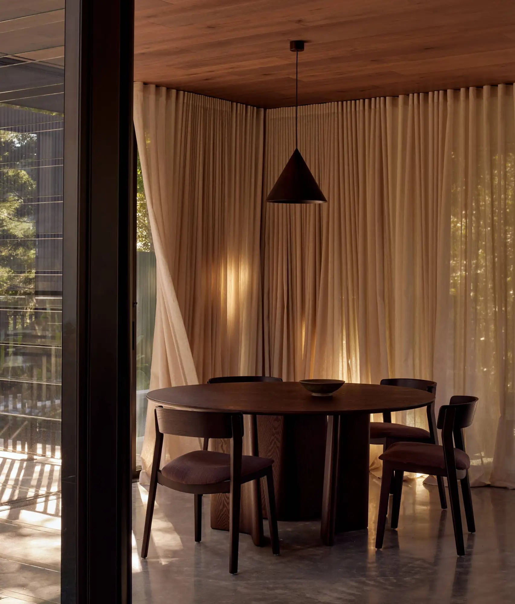 Dark wood round dining table with sleek, minimalist design and a central pedestal base.
