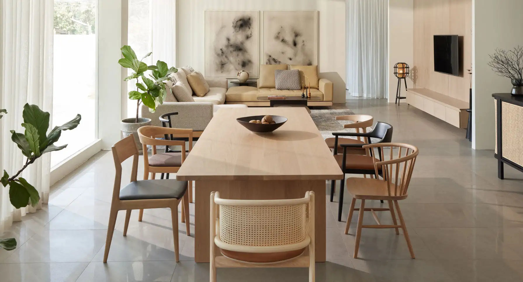 Long wooden dining table with a natural finish and minimalist design, surrounded by matching chairs featuring woven cane backs.