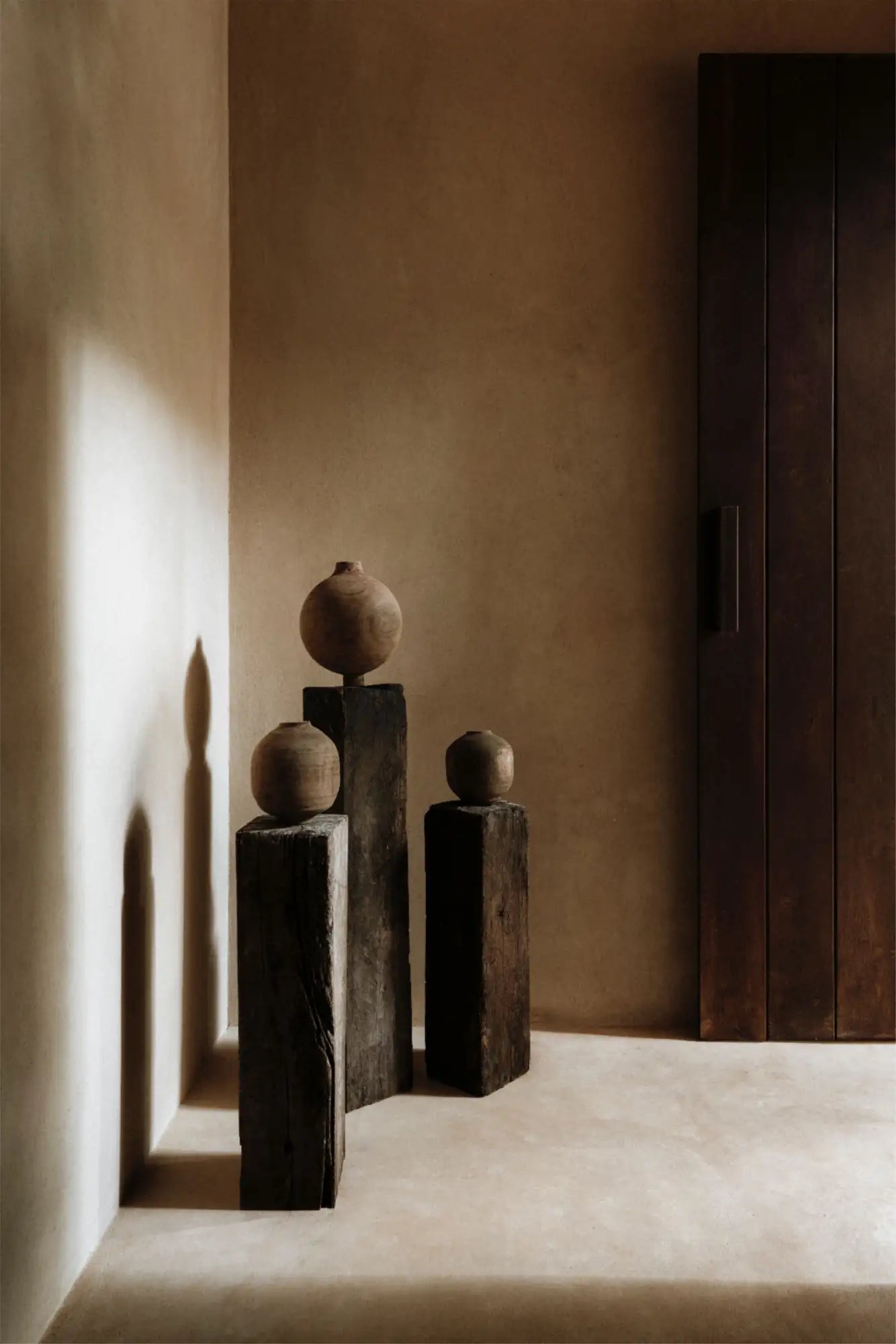 Three rustic terracotta spheres, each resting atop a dark wooden pedestal.